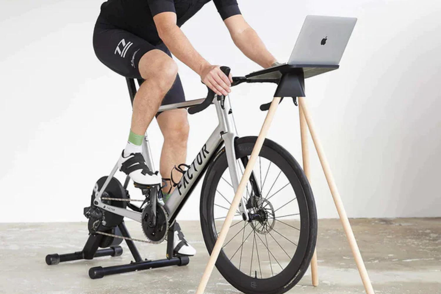 A man riding his bike indoor in front of a Tons Laptop table.